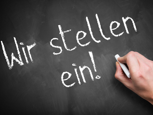 Auf eine Tafel werden mit Kreide die Worte „Wir stellen ein!“ geschrieben.