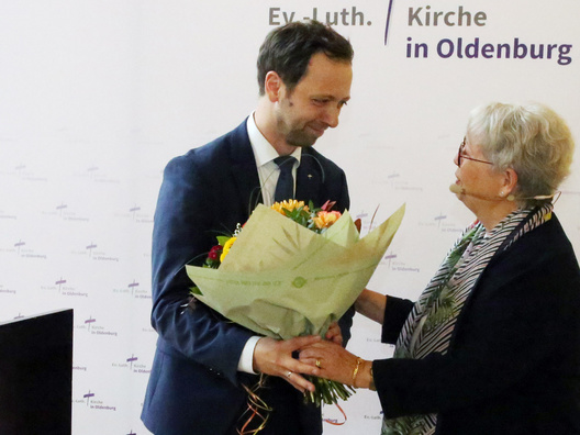 Oberkirchenrat Sebastian Groß wird ein Blumenstrauß von Synodenpräsidentin Sabine Blütchen überreicht.