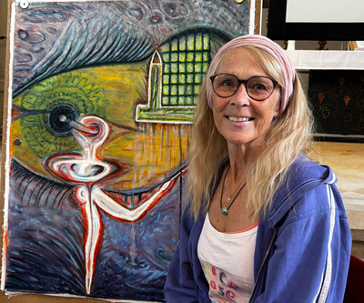 Zu sehen ist Barbara Tamminga, die ihre Erfahrungen und Emotionen in Collagen und Bildern künstlerisch bearbeitet hat. Hier vor dem Bild mit dem Titel: „Tanz am Meer“.
