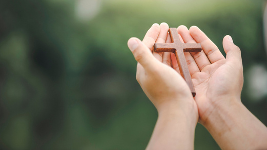 Hände halten ein Holzkreuz