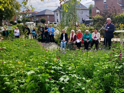 Menschen sitzen im Grünen auf Bänken, rechts im Bild steht Hans-Jürgen Hoffmann am Mikrofon und spricht.
