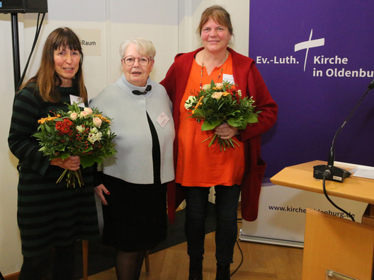 Drei Frauen stehen mit Blumensträußen im Raum.