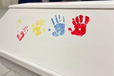 Eigene Sarggestaltung: Bunte Handabdrücke auf weißem Holz und einige Maus-Zeichnungen. 