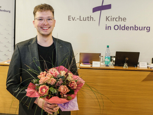 Chris Schellstede steht mit einem Blumenstrauß vor den Synodalen.