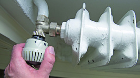 Thermostat an einer Heizung (Foto in CMYK) Eine Hand stellt die Temperatur an einer Heizung ein