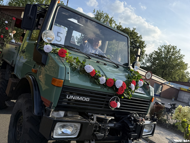 Der grüne Unimog, der den Wagen der Kirchengemeinde Westerstede / Ocholt zieht, ist mit einer rot-weißen Blumengirlande geschmückt.
