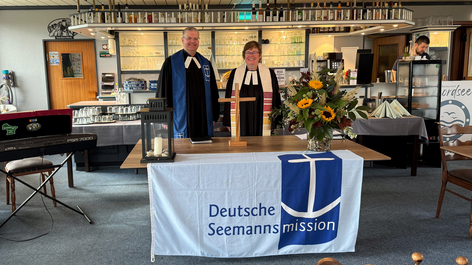 Zu sehen sind Pfarrerin Susanne Stephan (rechts) und Seemannspastor Dirk Jährig aus Brake (links) beim Seemannsgottesdienst im Restaurant Nordseeblick direkt am Hafen von Fedderwardersiel.
