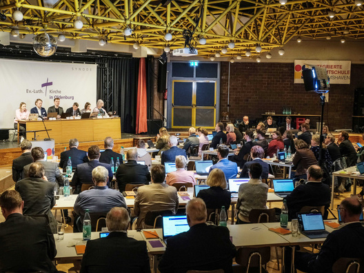 Viele Menschen sitzen im Saal und hören zu.