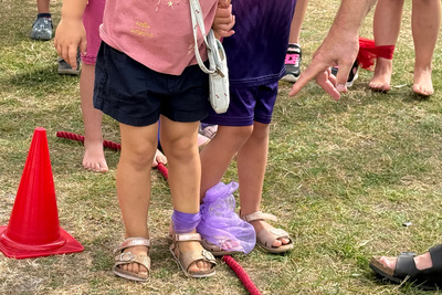 Zu sehen sind Kinderbeine, die zusammengebunden sind. Ein Beispiel für Freundschaft, wenn man aufeinander achtgibt.