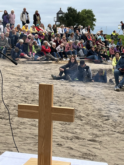 Viele Menschen nehmen am Strand von Dangast bei einer Andacht teil.