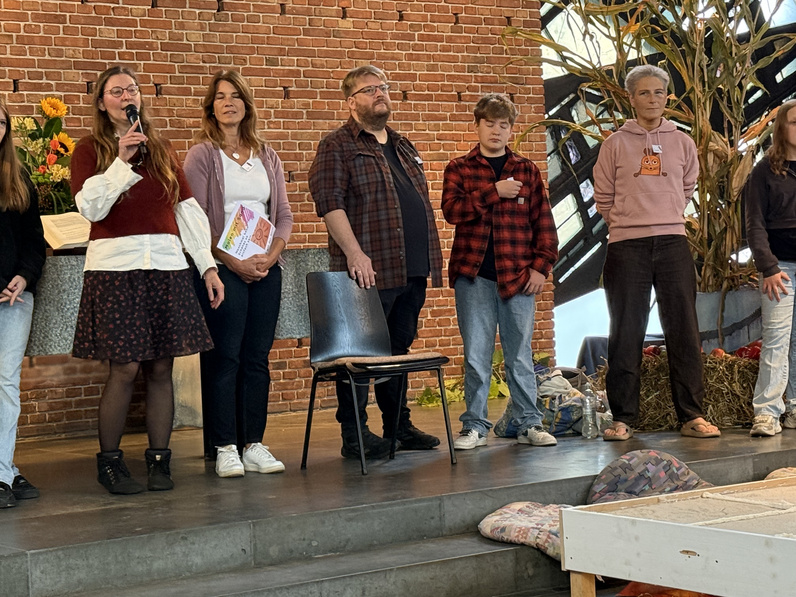 Vor dem Altar stehen fünf Menschen nebeneinander, Pastorin Sophie Ihne spricht ins Mikrofon.