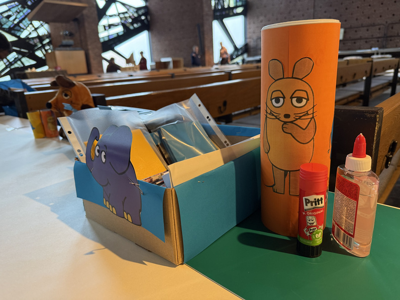 Auf einem Tisch stehen Bastelutensilien bereit - darauf geklebt sind Bilder von der Maus und dem Elefanten aus der "Sendung mit der Maus".