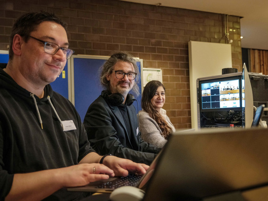 Drei Menschen sitzen vor PC und Technik