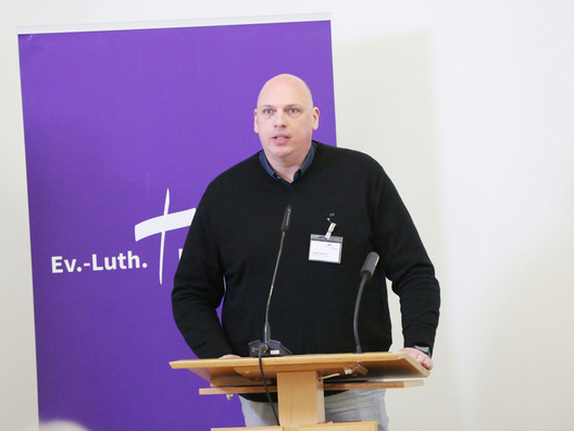 Auf diesem Bild ist Denis Goldner von der Mitarbeitendenvertretung bei seinem Statement der MAV zum Projekt zur Neustrukturierung der Verwaltung der Ev.-Luth. Kirche in Oldenburg zu sehen.