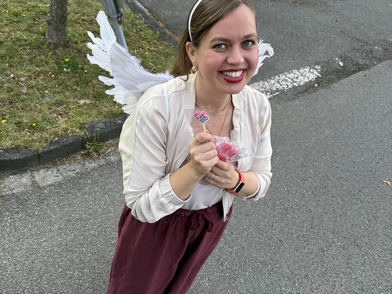 Von oben ist eine Ehrenamtliche fotografiert. In der Hand hält sie kleine rote Lollies, sie trägt kleine weiße Engelsflügel und einen kleinen Heiligenschein.