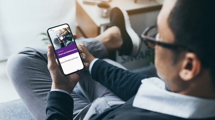 Ein Mann sitzt auf einem Sofa und liest Nachrichten auf einem Smartphone.