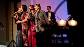 Fünf Personen stehen auf der Bühne, vier Frauen singen im Vordergrund.