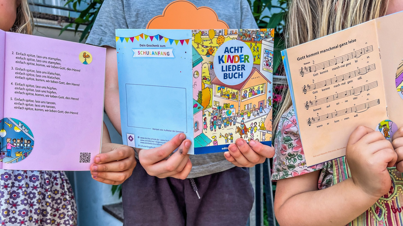 Drei Kinder halten das "AchtKinderliederbuch" in die Kamera