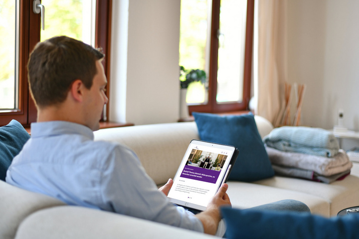 Mann sitzt auf einem Sofa und liest einen Newsletter auf einem Tablet.
