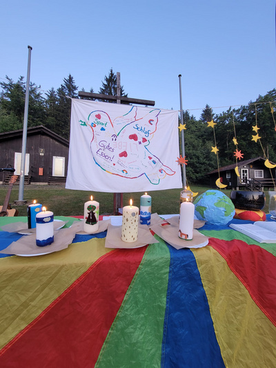 Auf einem bunten Tuch stehen Kerzen mit einer Friedenstaube auf einem Bettlaken darüber