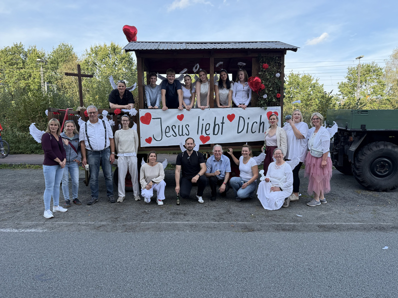 Gruppenfoto aller Beteiligten am Erntedank-Umzug vor dem Festwagen bei blauem Himmel.