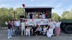 Gruppenfoto aller Beteiligten am Erntedank-Umzug vor dem Festwagen bei blauem Himmel.