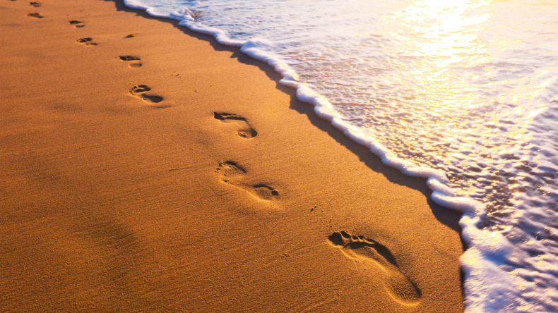 Sandstrand mit Spuren im Sand. Rechts daneben auslaufende Wellen des Meeres.
