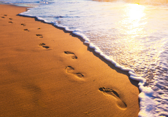 Sandstrand mit Spuren im Sand. Rechts daneben auslaufende Wellen des Meeres.