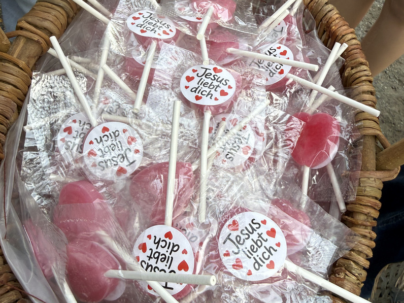 Ein Korb mit roten Lollies ist von oben abgebildet. Auf den Lollies steht "Jesus liebt dich".