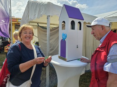 Eine Besucherin des Messezeltes steht neben dem lila Glockenturm und hält ihren gezogenen Segensspruch in der Hand.