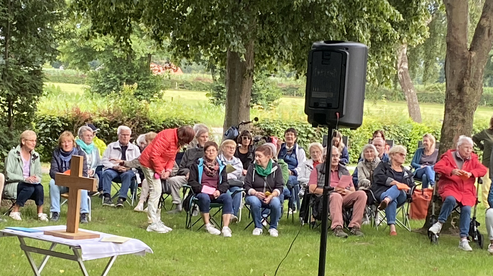 Menschen sitzen auf einer Wiese und warten auf die Andacht am Deich