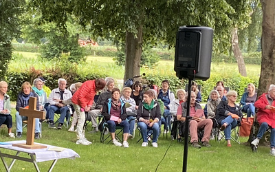 Menschen sitzen auf einer Wiese und warten auf die Andacht am Deich