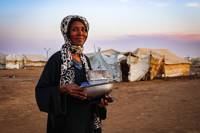 Zu sehen ist eine Frau im Sudan mit Artikeln des täglichen Bedarfs in den Händen.