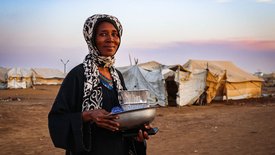 Zu sehen ist eine Frau im Sudan mit Artikeln des täglichen Bedarfs in den Händen.