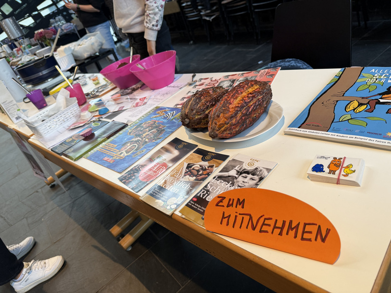 Von schräg oben ist ein Tisch fotografiert, auf dem verschiedene Hefte und zwei Brote liegen, daneben ein Schild auf dem "zum mitnehmen" steht.