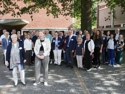 Eine Gruppe von Menschen steht draußen und schaut in die Kamera.