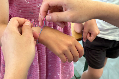 Zu sehen sind Kinder, die Freundschaftsbänder knüpfen.